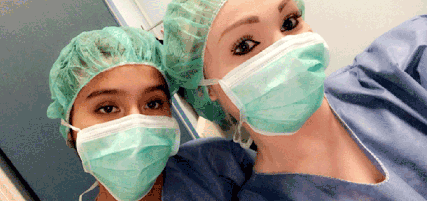Two students in surgical masks and caps take a picture together.