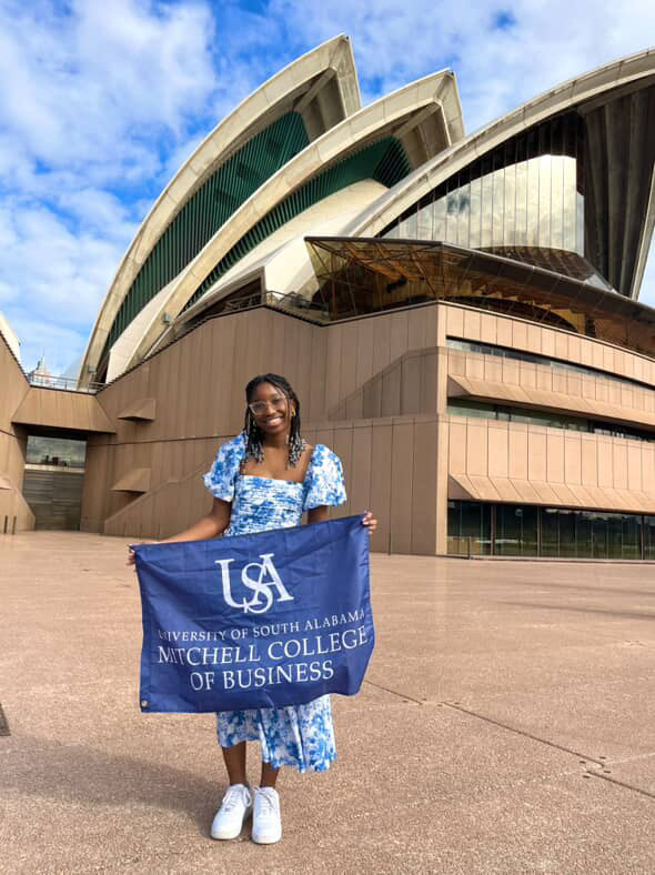 Sydney holds a College of Business flag in front of the Sydney Opera House