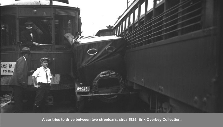 A car tries to drive between two streetcars, circa 1925.