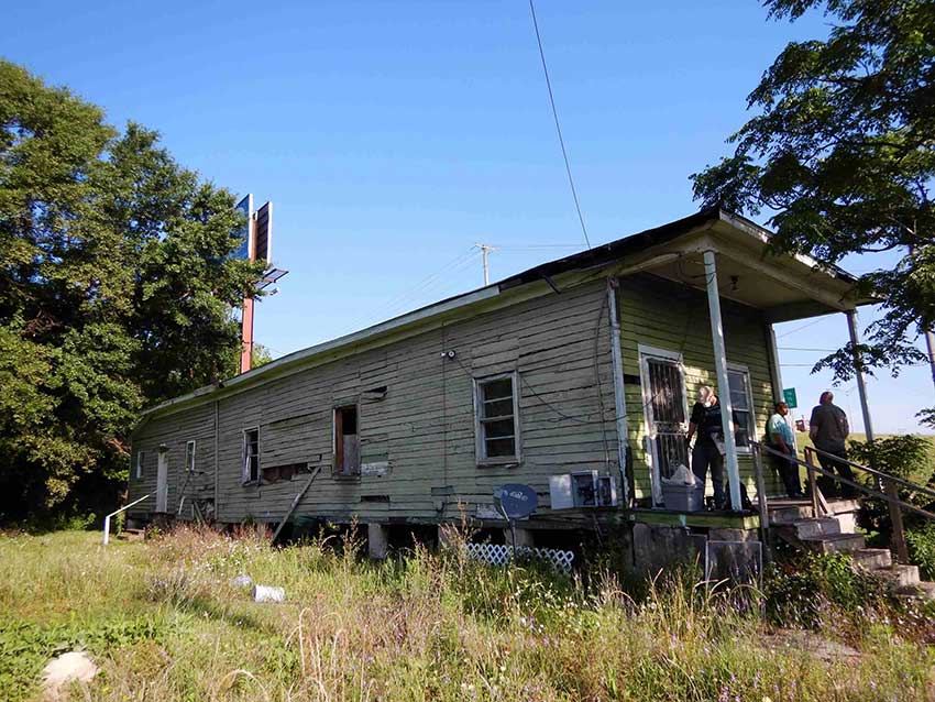 Light greens shotgun house with three people on the porch