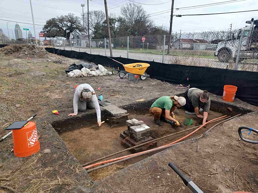 three archaeologists excavate a brick pier and utility lines