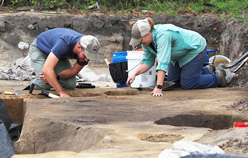 Emily Warner, right, with the USA Center for Archaeological Studies, and Thomas Grace, with Wiregrass Archaeological Consulting, bisect a feature in the soil at a site that is along the route for a proposed Mobile Bay bridge. 