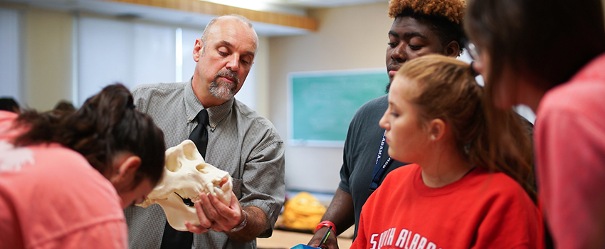 Dr. Carr holding skull showing to students in classroom.
