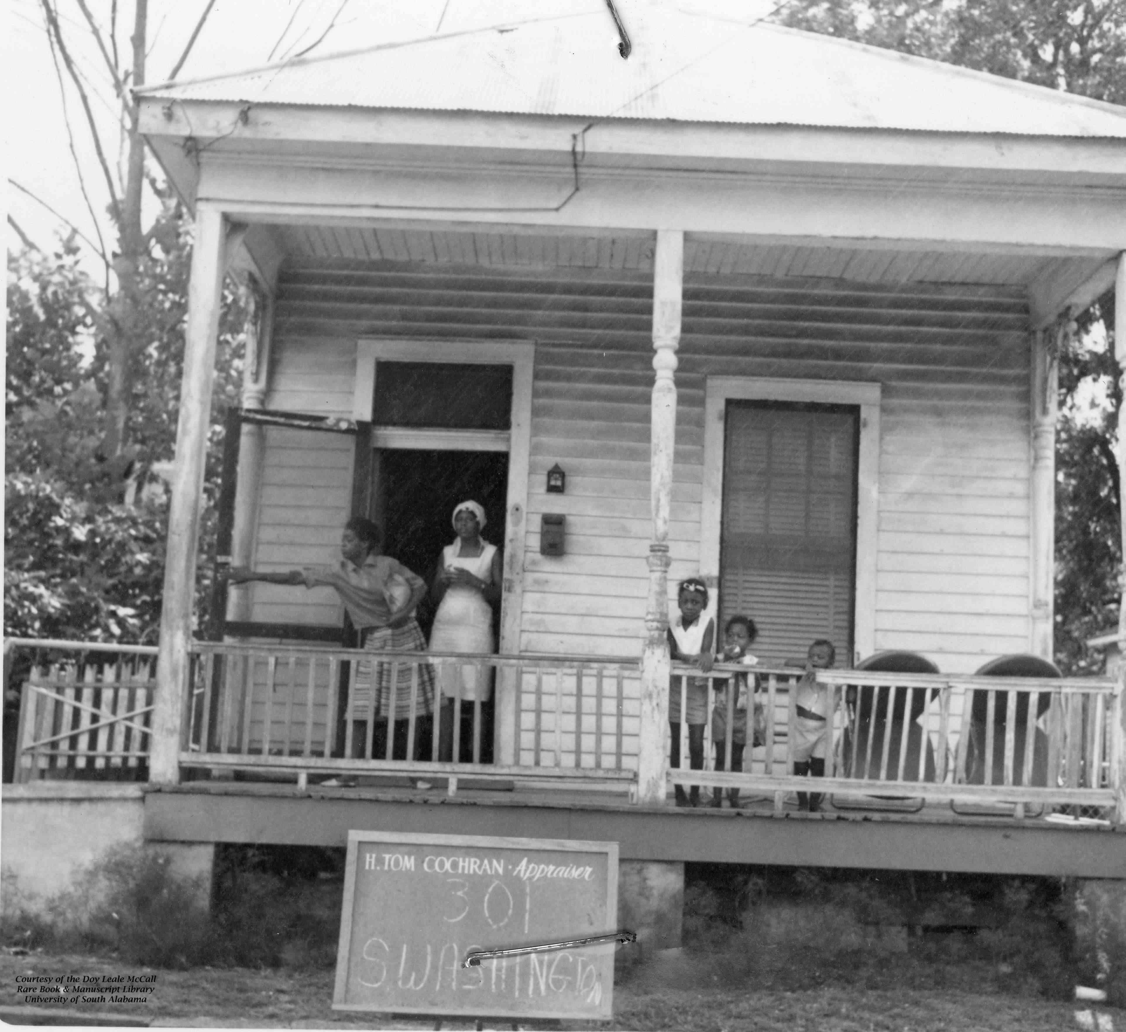 Women and children stand on a porch in a black and white photo