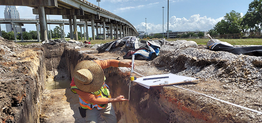 An archaeologist measures layers of soil in a trench for the I-10 Mobile River Bridge Archaeological Project.