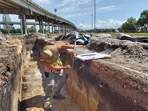 An archaeologist measures layers of soil in a trench for the I-10 Mobile River Bridge Archaeological Project.