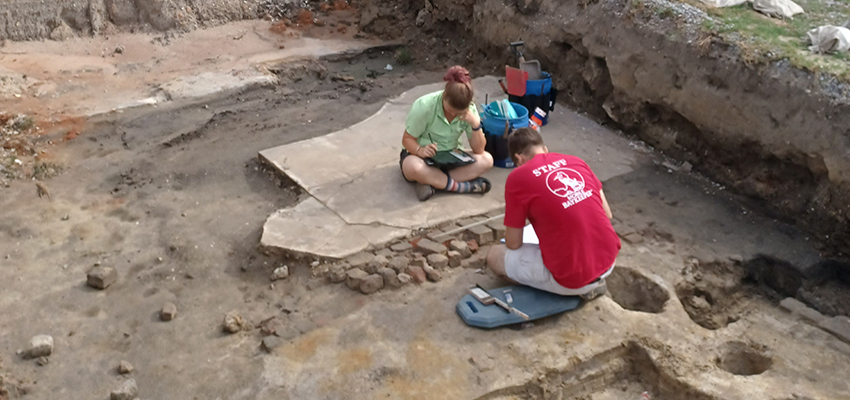 Lindsey and Richard map features at the former street level at the South Royal Street Site. Lindsey is sitting on the former sidewalk, and Richard is measuring bricks from a porch foundation.